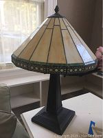 Full view of the Tiffany style table lamp showing the cream and green stained glass shade and dark metal base on a white table near a window.