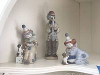 Three Lladro clown figurines displayed together on a shelf.
