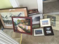 Overview of various framed paintings, photos, and canvases arranged on floor and leaning against wall.