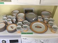 Full set of Dansk Fiance Fruits dinnerware displayed on a counter including cups, saucers, mugs, plates, bowls, and serving pieces.