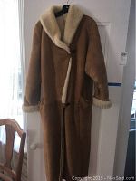 Full-length view of tan sheepskin coat showing shearling collar and cuff trim hanging on door.