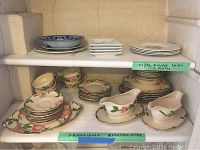 Shelf with 4 Royal Dalton china plates (top right) and blue floral plates (top left) and multiple pieces of Franciscan Earthenware including cups, saucers, plates, and gravy boats on the lower shelf.