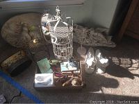 Full view of lot items including metal birdcage, carved wooden plaques, metal bird stand, ceramic birds, and other decorative items on carpet.