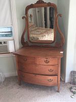 Full view of the vintage wooden dresser with attached ornate framed mirror in a bedroom setting.