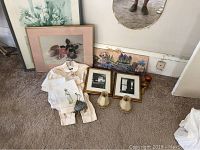 Photo showing vintage child's suit, small handbag, and several framed art pieces on the floor under a wall mirror.