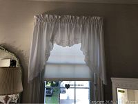 Photo of a white fabric valance with ruched top and embroidered scalloped bottom edges hung above a window showing outside view.
