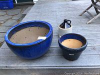 Four blue ceramic planters of varying sizes and one brown ceramic jug arranged on deck outdoors.