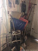 Photo showing snow shovels, push brooms, rake, and aluminum walker leaning against barn wall