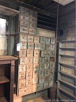 Full view of the teal painted solid wood antique card catalog mounted on a wall with many small drawers.