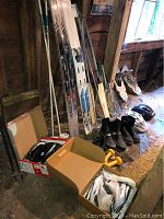 Photo showing skis, ski poles, boots, helmets, snowshoes, and tennis rackets arranged in barn