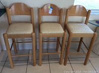 Set of three matching wooden bar stools lined up side by side showing front view and fabric seats.