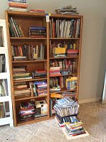 Front view of solid wood bookshelf filled with books and magazines, showing adjustable shelving and natural wood finish.