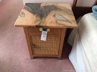 Full view of the nightstand with marble top placed on it. Nightstand has a wooden frame with metal feet and a woven rattan or wicker panel on the door.
