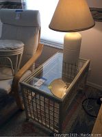 Side view showing white cushioned chair, glass-top rattan side table, and ceramic lamp with shade turned on showing lamp is working.
