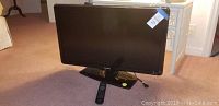 Front view of the 32" Philips TV on its stand with remote beside it on the floor.