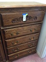 Full view of dark wood dresser with carved floral detail on top drawer and brass handles on four drawers.