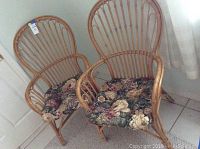 Two rattan chairs with floral patterned cushions placed side by side on a tiled floor near a door.