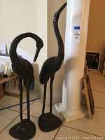 Front view showing both crane sculptures side by side with pillar in background.