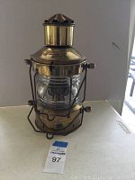 Full view of the polished brass ships oil lamp with glass globe and metal frame handle.