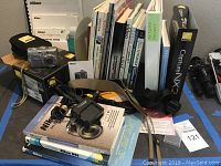 Overview of Nikon camera, books, manuals, tripod, camera accessories, and cleaning supplies arranged on a table.