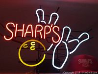 Full view of neon sign showing 'SHARP'S' text in red with bowling ball in yellow and bowling pins in white, mounted on black stand.