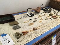 Overview of varied men's accessories including belt buckles, cuff links, tie tacks, a lariate, scissors, and a wooden shoe form laid on a crochet tablecloth