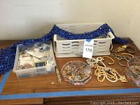Wide view of assorted jewelry, blue sequined shawl, and plastic storage containers on a table