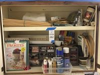 Wide photo showing the overall assortment of craft supplies organized on shelving, including paint bottles, spray adhesives, wooden dowels, crafting magazines, beads, and organizer bins with smaller craft items.