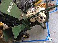Full view of green painted steel chipper shredded unit with hopper, discharge chute and wheels