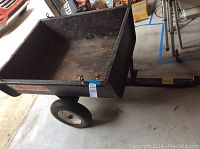 Full side view of the Snapper lawn mower trailer showing the rectangular metal bed with some surface rust, black painted exterior, two pneumatic tires with white rims, and hitch attachment at the front.