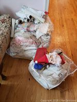 Two large clear bags filled with folded and rolled table linens and runners; white, floral, lace and pastel prints visible.
