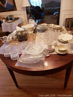Wide shot of entire lot on wooden oval table with various porcelain and glass pieces visible.
