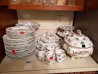 Overall view of stacked dinner and salad plates, bowls, teacups, tureen, and serving platters showing floral pattern and gold trim.