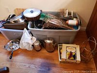 Wide shot showing bins filled with metal pots, pans, baking trays, and kettles alongside drying racks, cutting boards, and plastic containers.