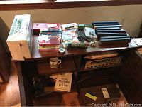 Overview photo showing plastic train cars, track pieces, metal train cars in cases, train books and mug on a wooden cabinet.