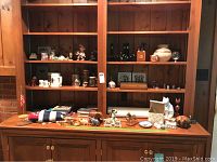 Wide view showing wooden cabinet shelves with decorative beer steins, miniature animals, books and other small collectible items.