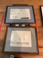 Framed sketches and prints of ships and boats, two pieces shown in full on wooden floor.