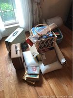Photo showing sewing machine cases, crates with fabrics and sewing supplies under window with natural light