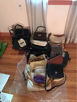 Full view of various handbags and purses arranged on floor in front of curtain.