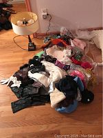 Wide view showing a pile of scarves, gloves, hats, and other assorted accessories on a floor beside a lamp.