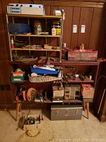 Wide shot of wooden shelving and workbench holding assorted vintage hand tools, electrical sander, circular saw, glue bottles, steel wool, and storage boxes.