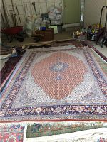 Full view of the large area rug rolled out on the floor showing overall pattern and colors, with background of storage and other household items.