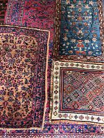 Four small area rugs with various patterns and colors on a larger patterned rug base; visible wear and frayed edges