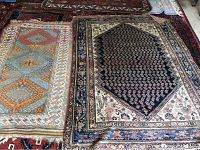 Photo showing two area rugs laid out side by side, one with a navy blue central medallion and floral border, the other with a bright geometric design and frayed fringe.