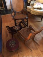 Photo of large wood rocker with cane seat and back, child's cane rocker, needlepoint footstool with side handles, and round needlepoint stool on wood floor near sofa.