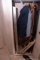 Photo showing the aluminum folding ladder beside hanging clothes, also showing the white folding step stool folded and leaning against the wall.