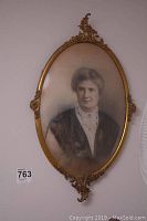 Full view of the oval portrait showing ornate metal frame and photograph of the woman.