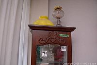 Top of wooden cabinet showing three glass oil lamps including a large yellow ribbed glass lamp shade and one clear glass oil lamp with brass burner and chimney.