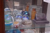 Front view of various glass paperweights including floral spheres, iridescent orbs, amber bottle and glass blocks