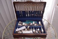 Full view of wooden flatware box holding silver plated cutlery organized in slots and loose in the box bottom under natural daylight.